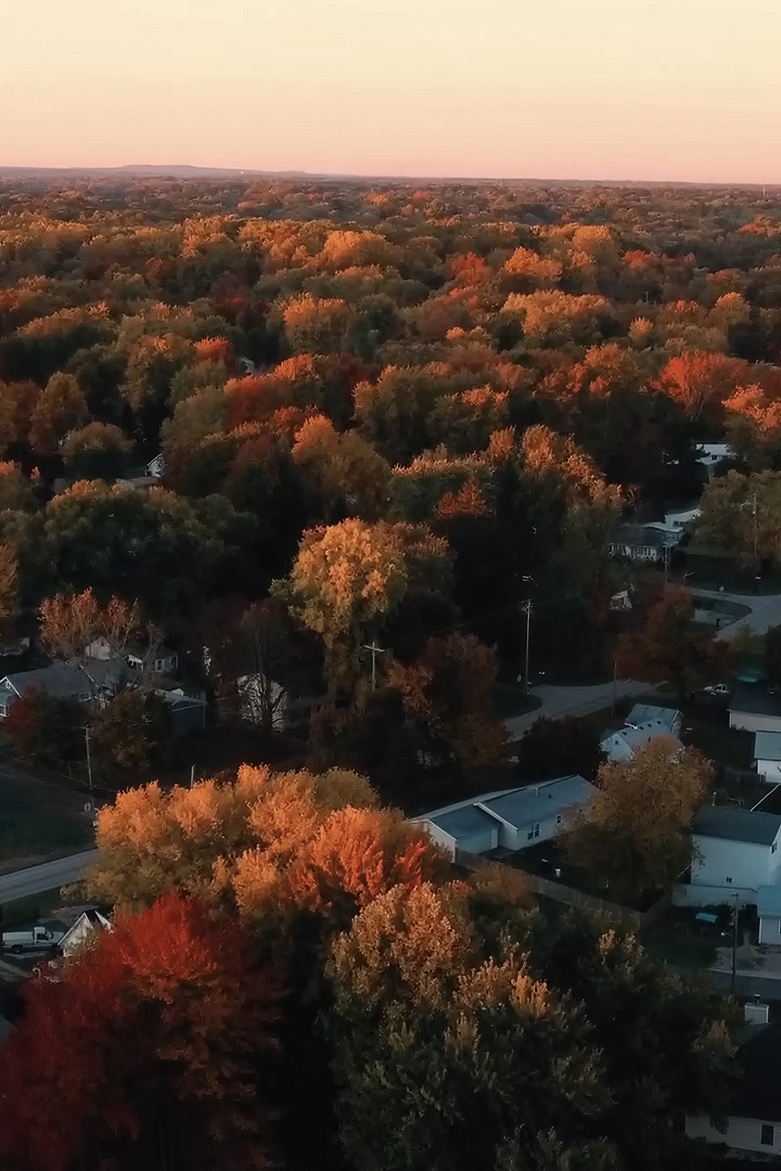 Autumn treetops in orange and red across Madison, Ohio, seen from above at sunset